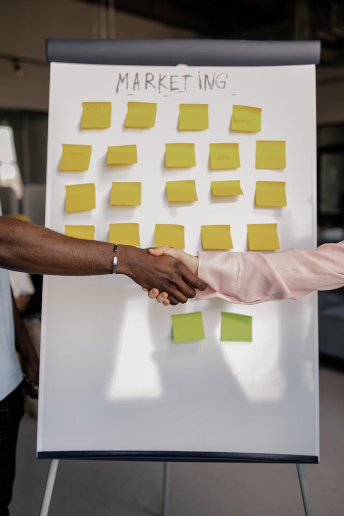 about-02 Colleagues shaking hands in front of a marketing board during a business meeting.